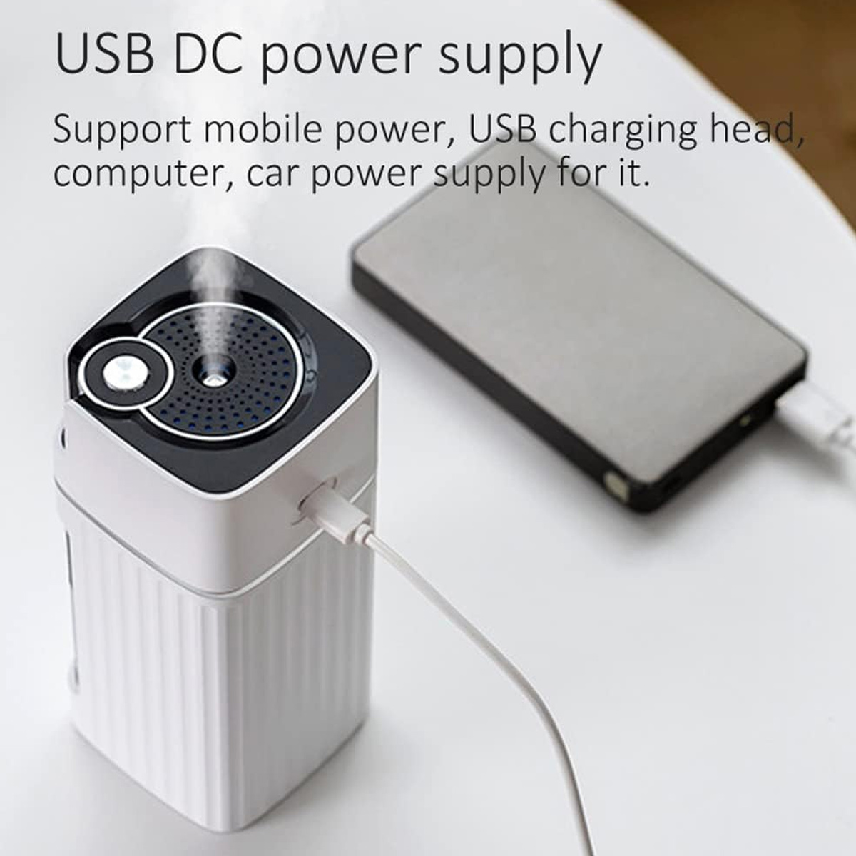 Ein weiß-schwarzer Luftbefeuchter mit USB-Kabel neben einer grauen Powerbank. Dampf tritt aus dem Luftbefeuchter aus.