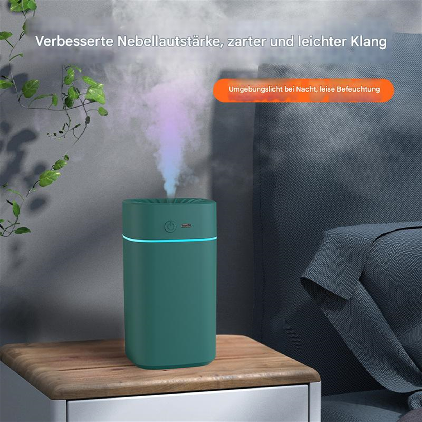Grüner Luftbefeuchter mit Nebel auf einem Holztisch. Grüne Blätter daneben, vor grauer Wand und blauem Stoff.