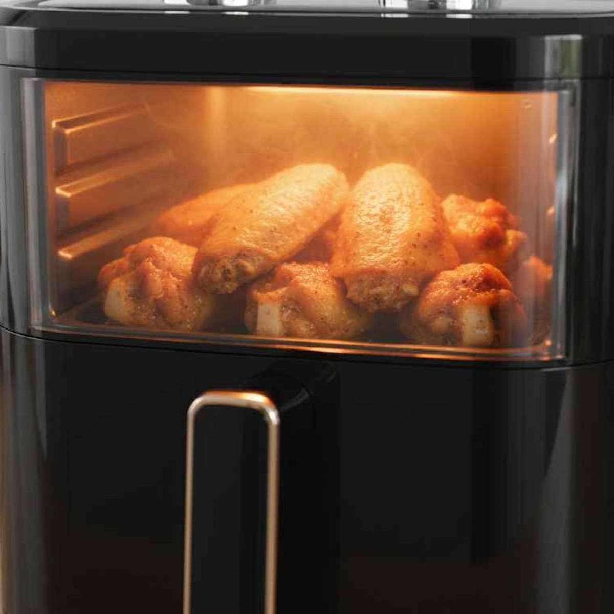 Eine Heißluftfritteuse mit Hähnchenflügeln im Inneren. Die Flügel sind goldbraun, und die Fritteuse ist schwarz mit einem durchsichtigen Fenster.