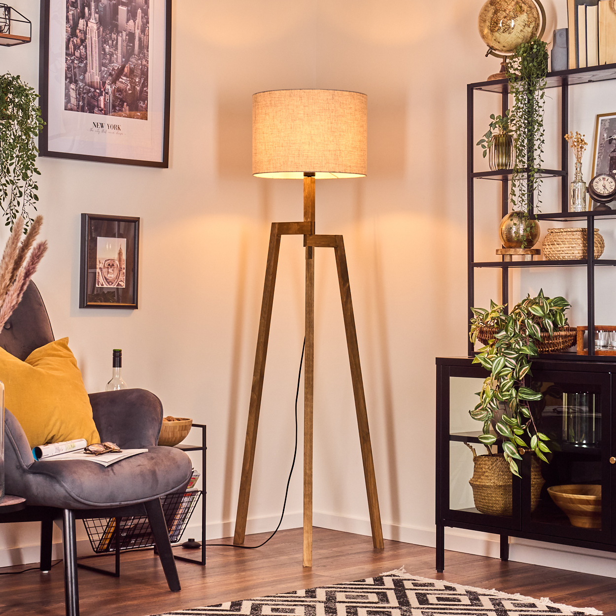 Ein Raum mit einer hölzernen Stehlampe. Links ein grauer Sessel mit gelbem Kissen. Rechts ein Schrank und ein Regal.