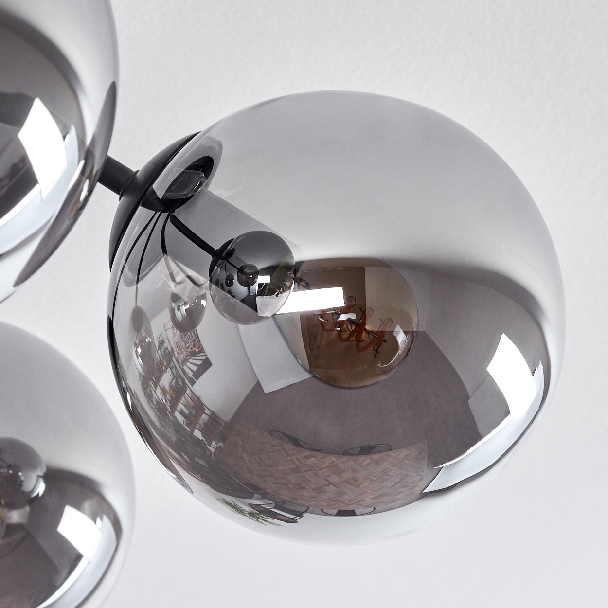 Eine moderne Deckenleuchte mit mehreren grauen Glaskugellampen, die einen Raum reflektieren. Die Glühbirnen sind im Inneren der Kugeln sichtbar.
