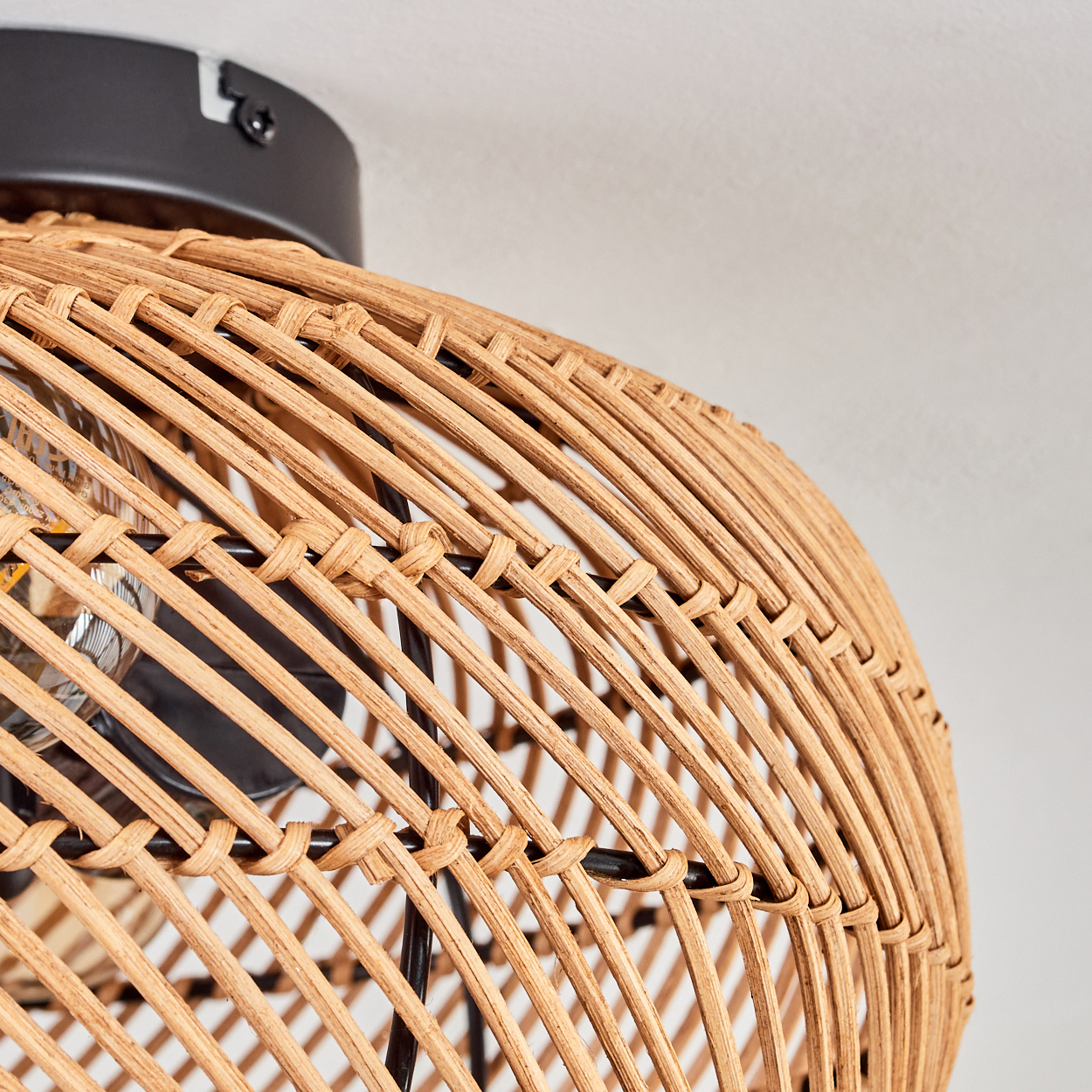 Nahaufnahme eines gewebten Lampenschirms aus Rattan. Der Lampenschirm ist hellbraun, mit einem schwarzen Metallrahmen und einer Glühbirne.