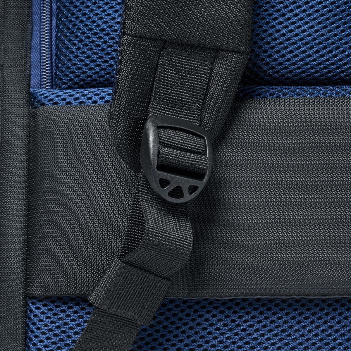 Nahaufnahme eines schwarzen Rucksackgurts mit Schnalle, vor blauem Mesh und dunklem Stoffhintergrund.