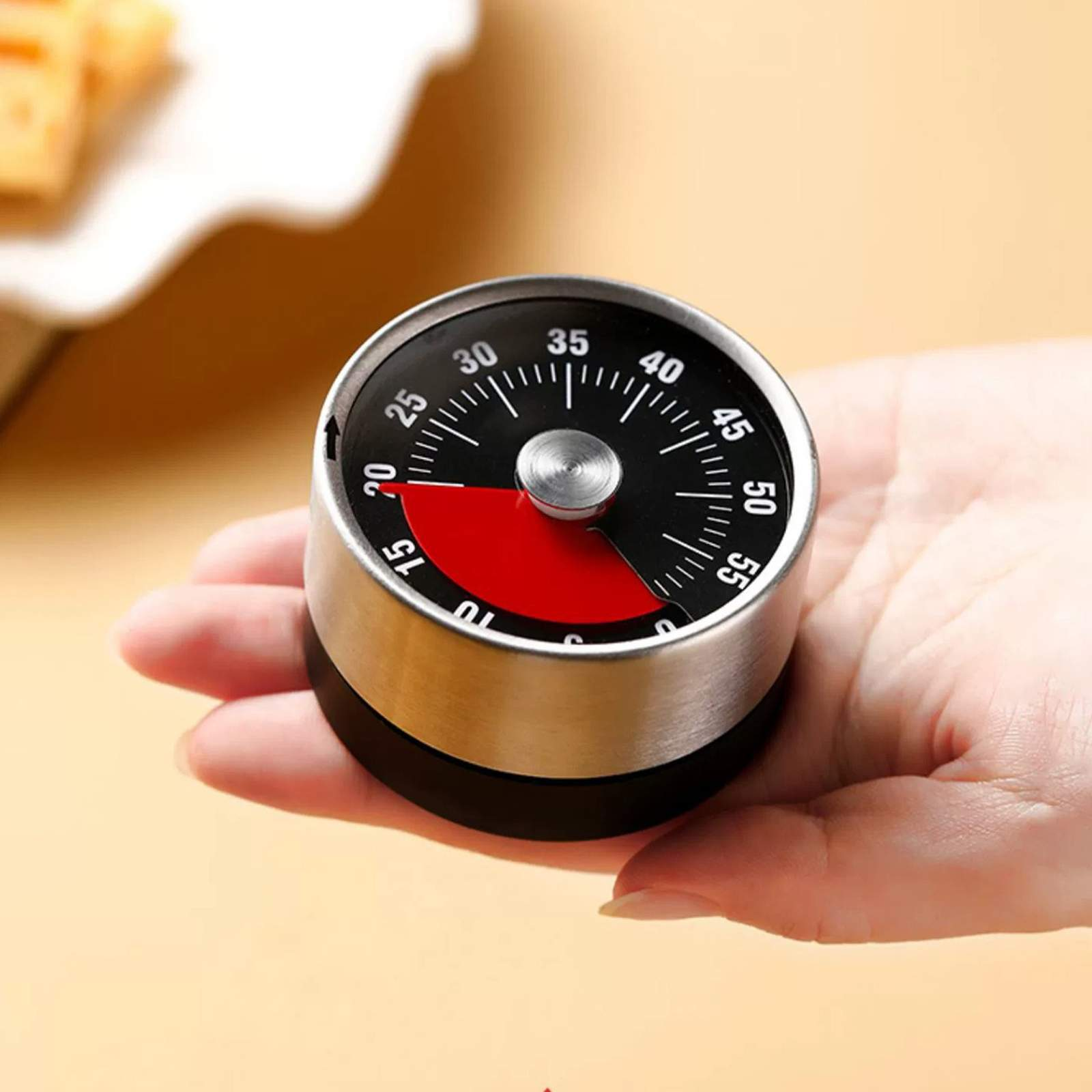 Ein Timer, der von einer Hand gehalten wird. Er ist rund, schwarz mit weißen Zahlen und hat ein rotes Segment, das die Zeit anzeigt.