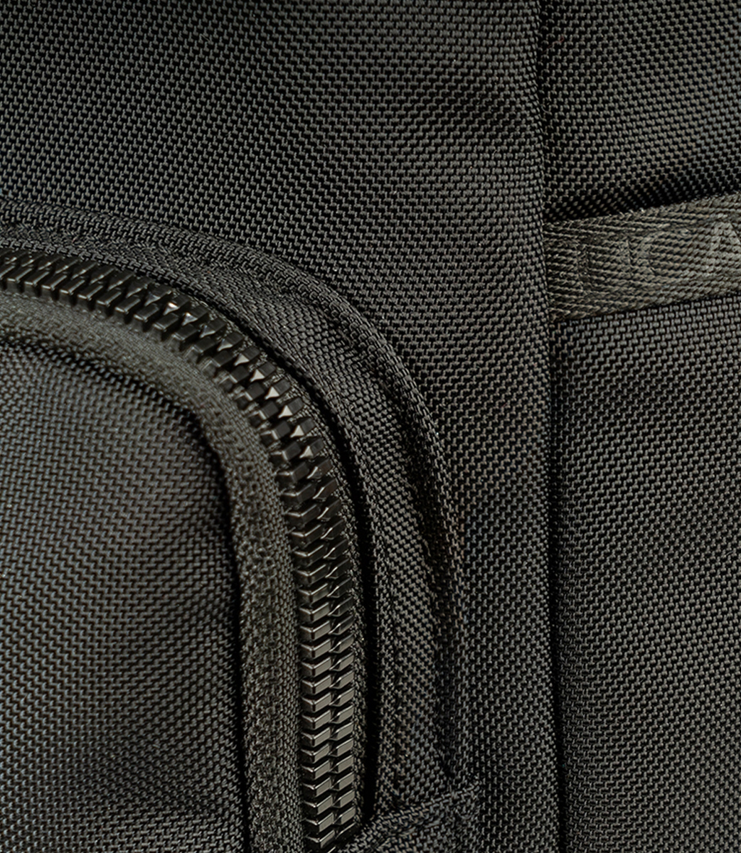 Nahaufnahme eines schwarzen Nylongewebes. Sichtbar sind ein Reißverschluss, eine gebogene Tasche und die Textur des Materials. Es gibt einen Markennamen.