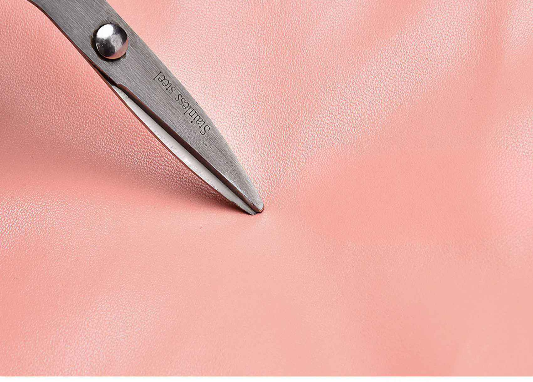 Schere auf rosa Oberfläche. Die Schere ist silberfarben und die Oberfläche ist ein strukturiertes Rosa. Die Klingen sind nah an der Oberfläche.