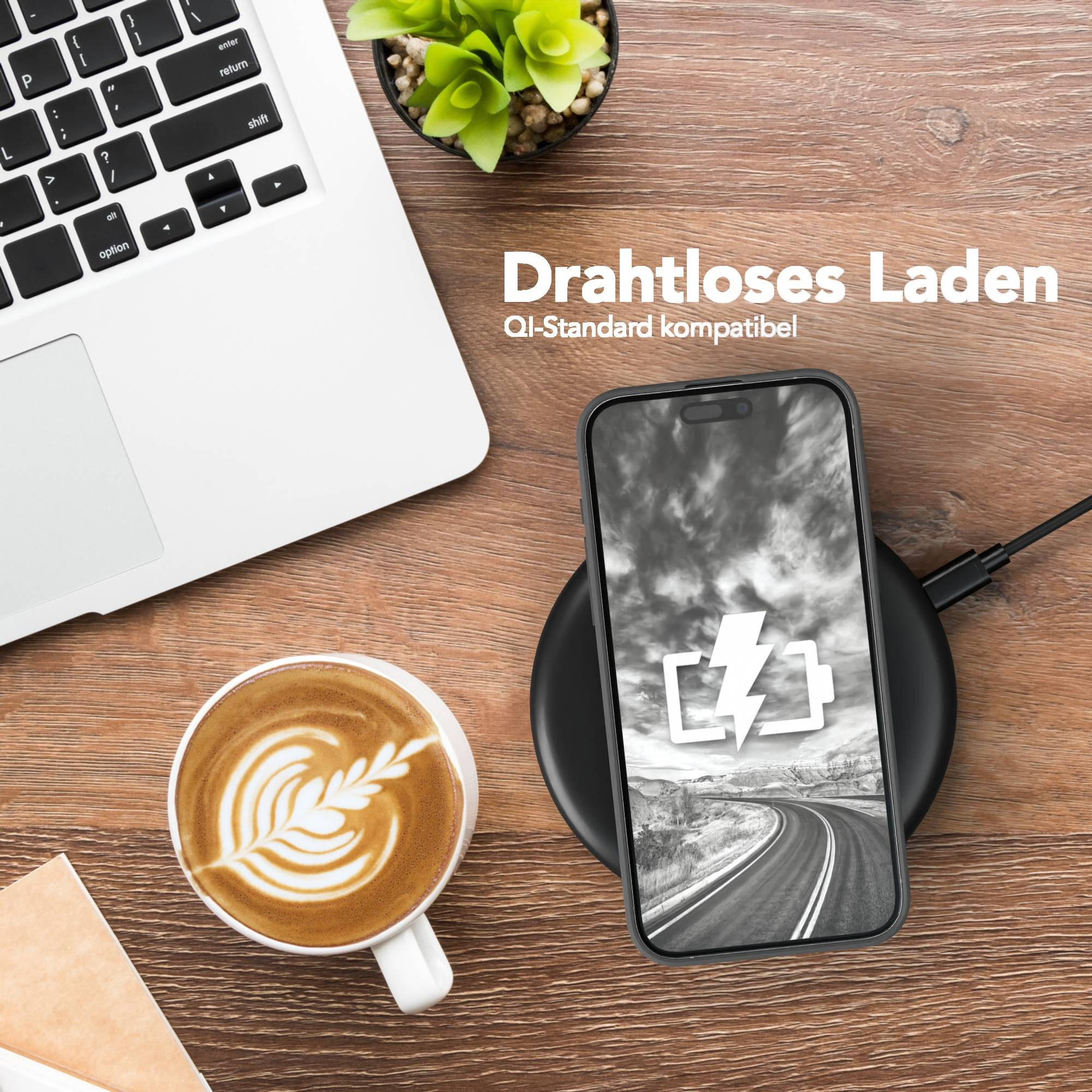 Ein Telefon, das drahtlos auf einem Pad geladen wird. Ein Laptop, eine Kaffeetasse und eine Pflanze befinden sich auf einer Holzoberfläche.
