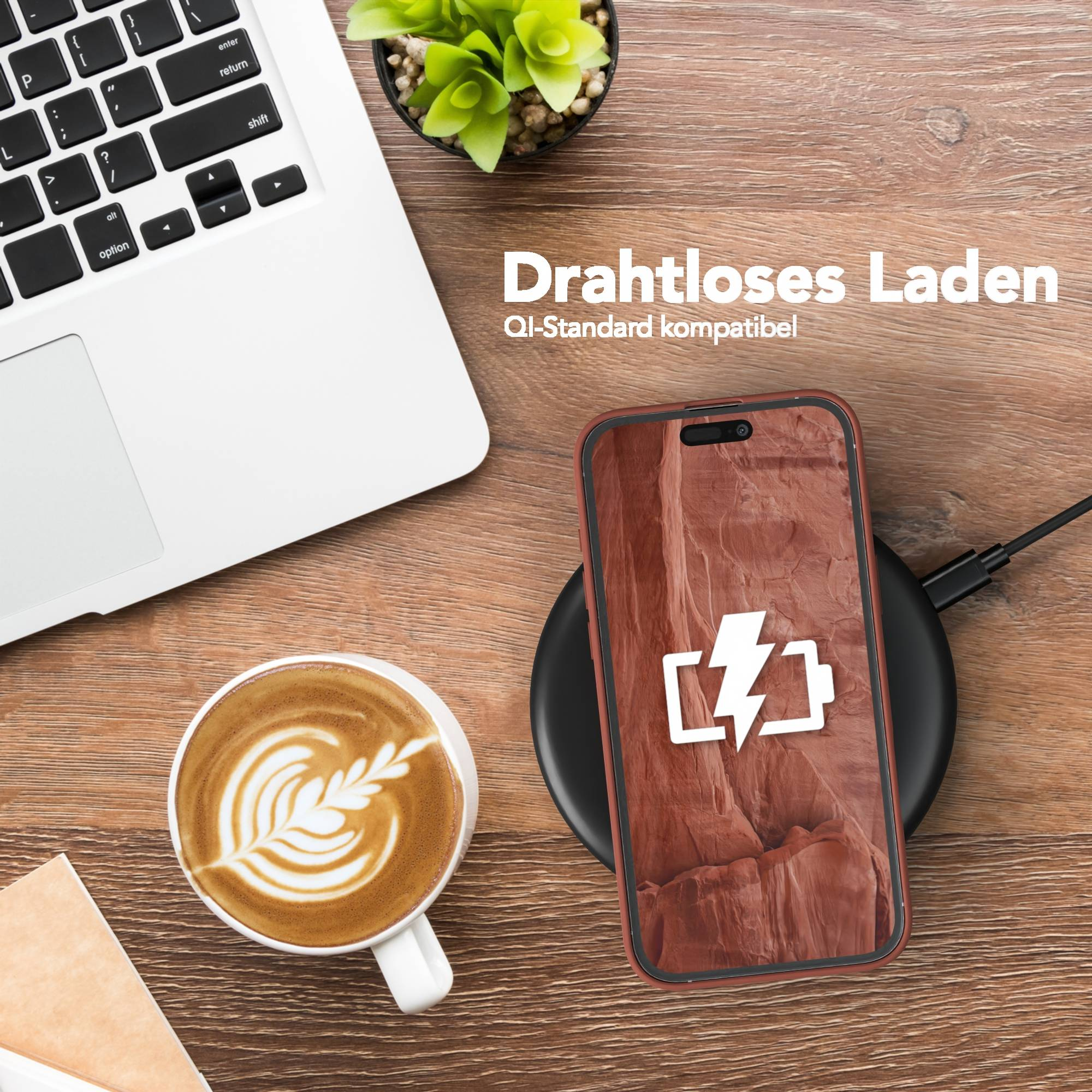 Ein Telefon, das drahtlos auf einem Pad geladen wird. Ein Laptop, Kaffee und eine kleine Pflanze sind ebenfalls auf einem Holztisch.