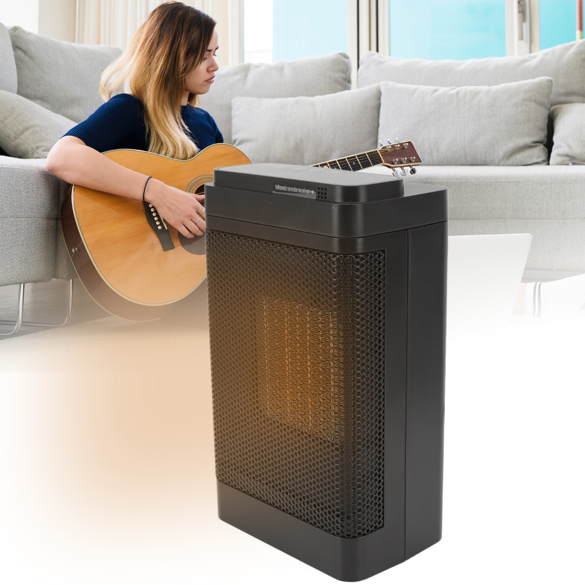 Eine Frau spielt Gitarre in der Nähe eines schwarzen Heizgeräts. Im Hintergrund sind ein graues Sofa und Kissen sowie ein Fenster zu sehen.