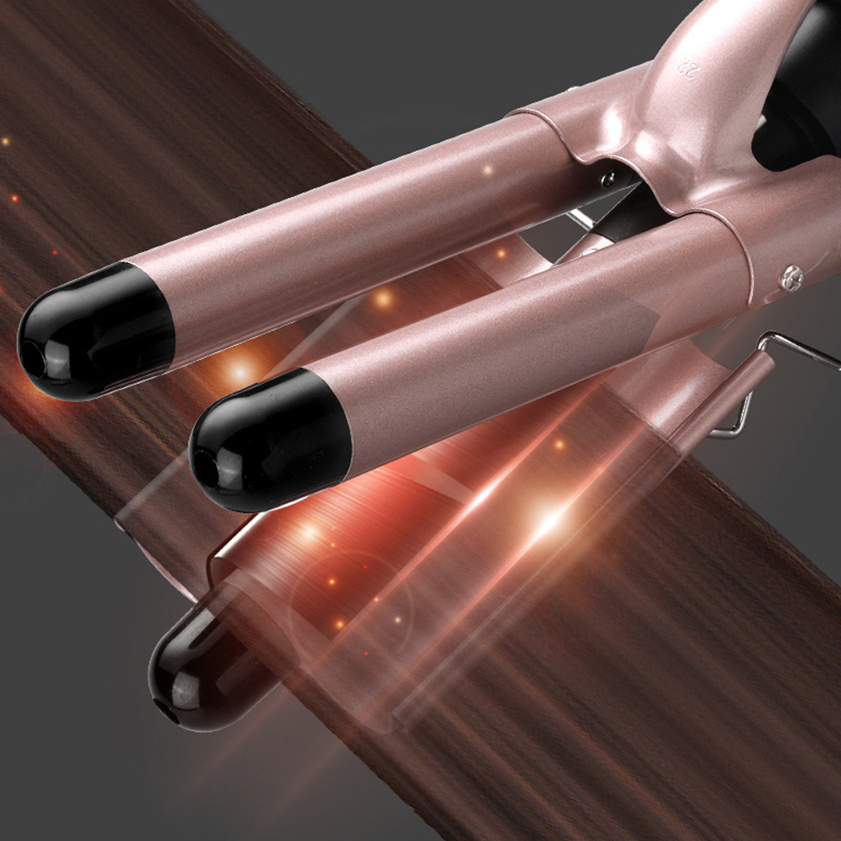 Nahaufnahme eines roségoldenen Lockenstabes mit schwarzen Spitzen über braunem Haar. Lichtreflexe erzeugen einen dynamischen Effekt.