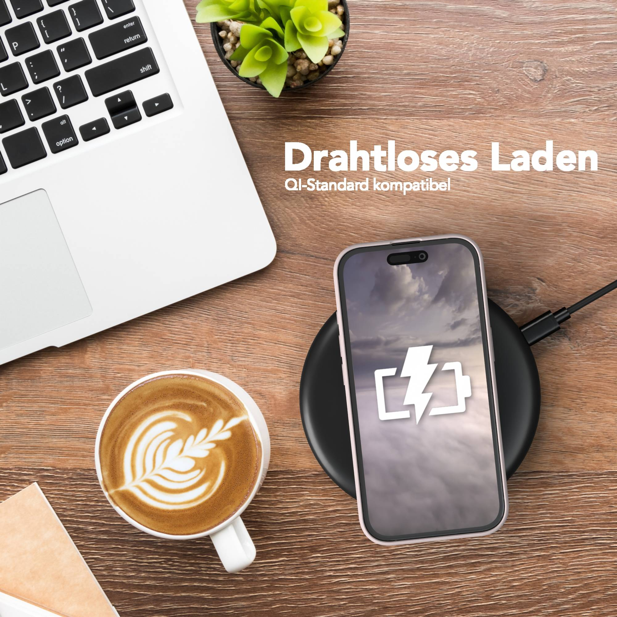 Ein Telefon, das drahtlos auf einem Pad aufgeladen wird, neben einem Laptop und Kaffee. Das Telefon zeigt ein Batteriesymbol an.