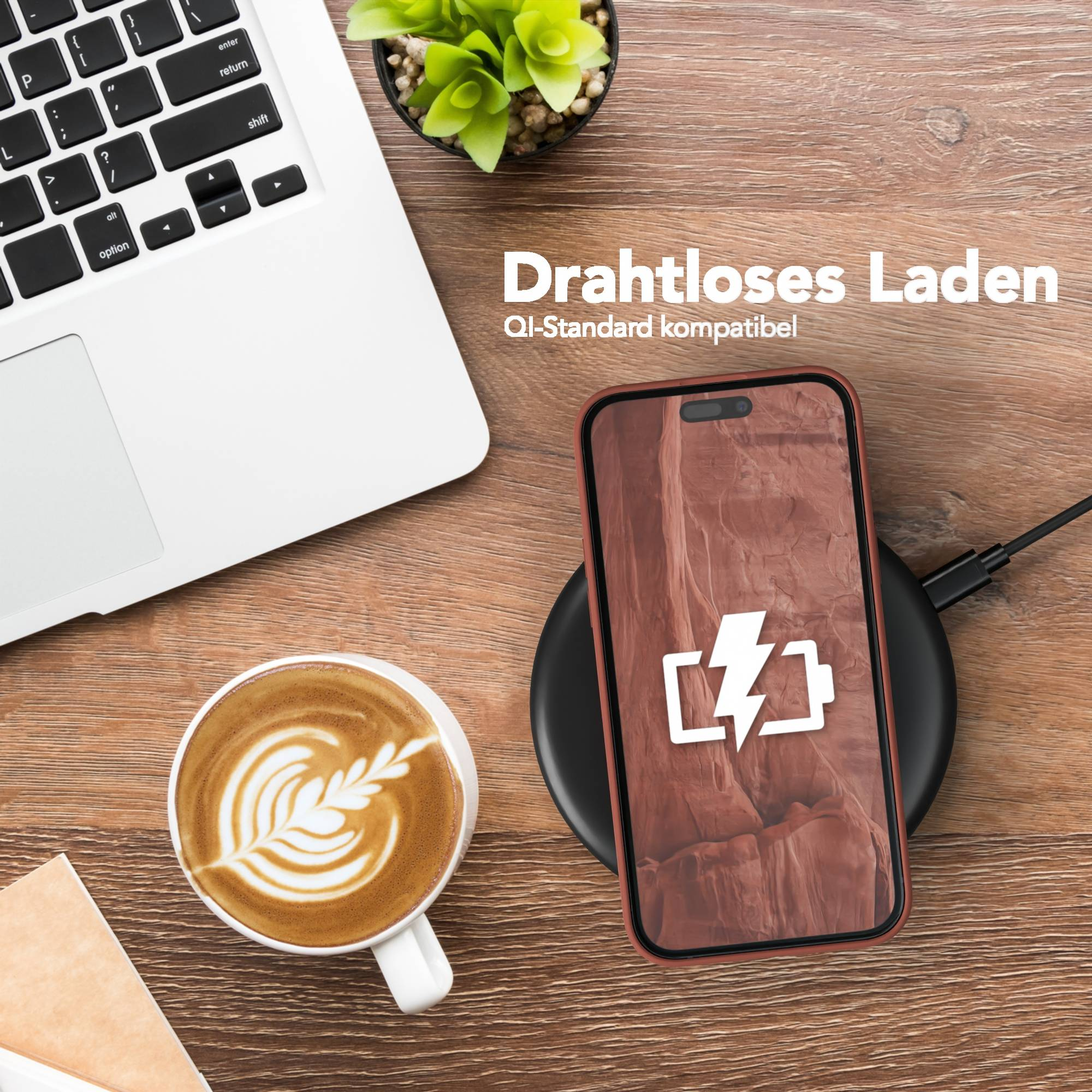 Ein Telefon, das drahtlos auf einem schwarzen Pad geladen wird, mit einem Latte, einem Laptop und einer Pflanze.