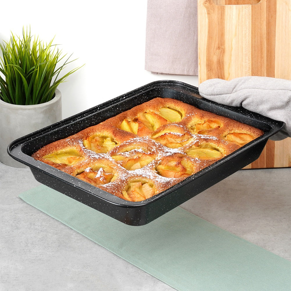 Tarta de manzana en una bandeja para hornear negra. La tarta está espolvoreada con azúcar glas. Una mano con un guante sostiene la bandeja.