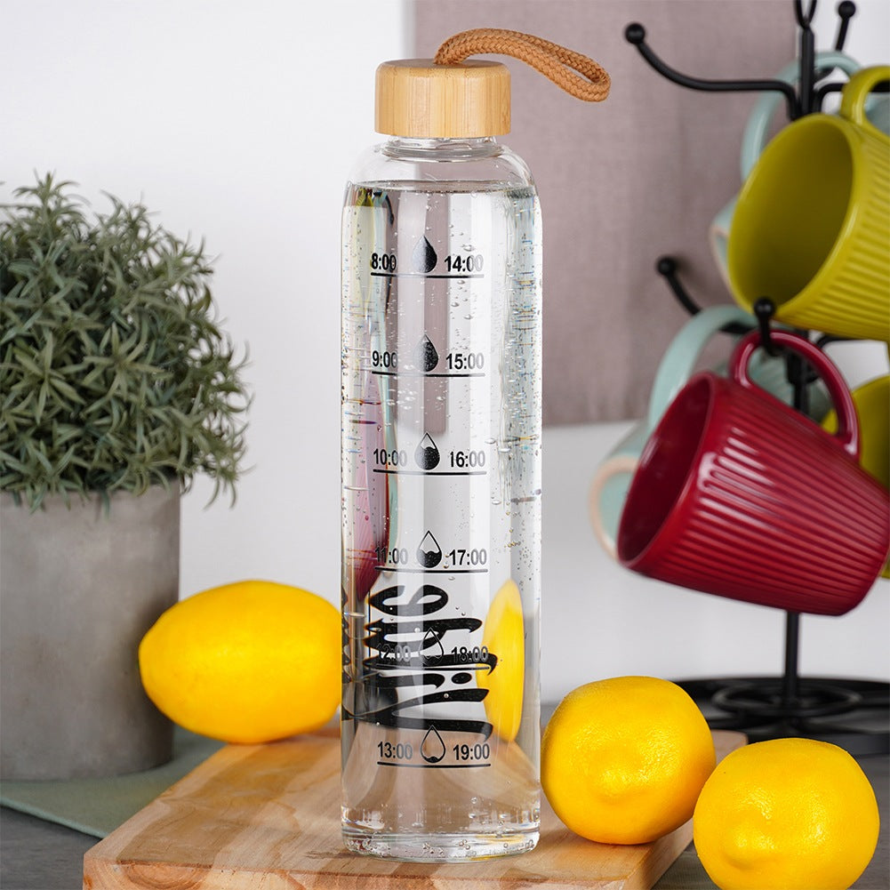Una botella de agua transparente con marcas horarias. Limones, una planta en maceta y tazas coloridas visibles al fondo.