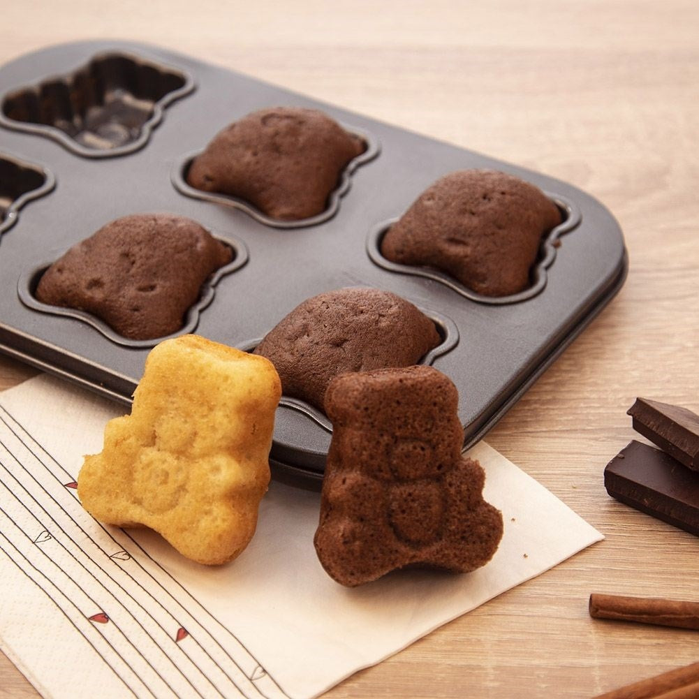 Pasteles con forma de oso de peluche, algunos en una bandeja, uno en una servilleta, con chocolate y canela sobre madera.