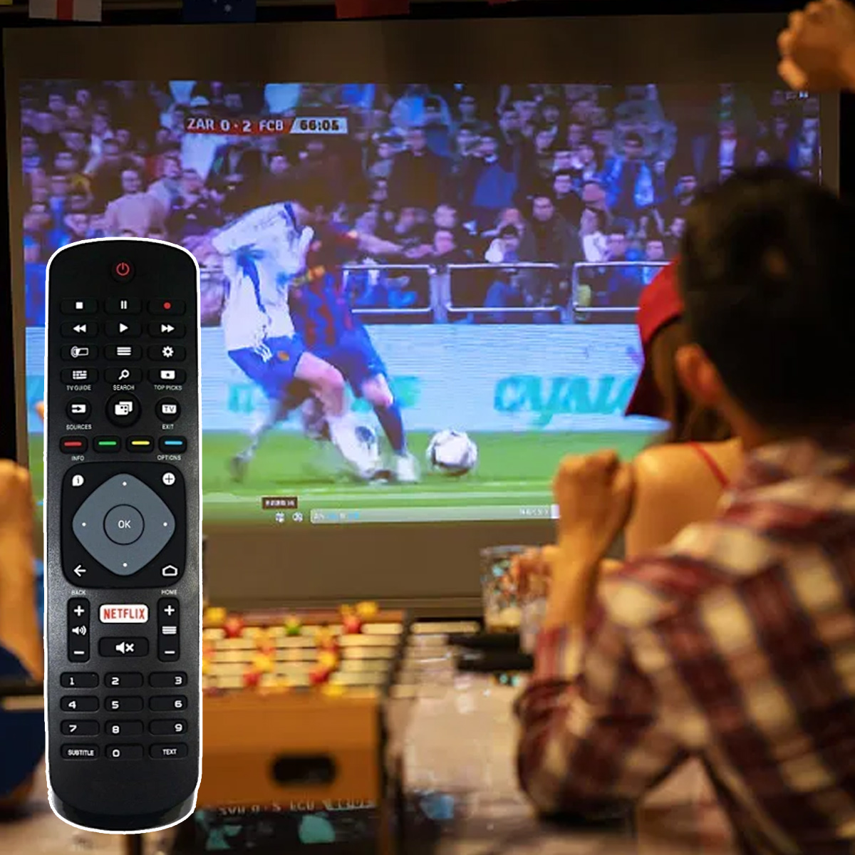 Menschen schauen ein Fußballspiel im Fernsehen. Eine Fernbedienung ist im Vordergrund. Das Spiel zeigt Spieler und einen Ball. Menschen sind im Hintergrund.
