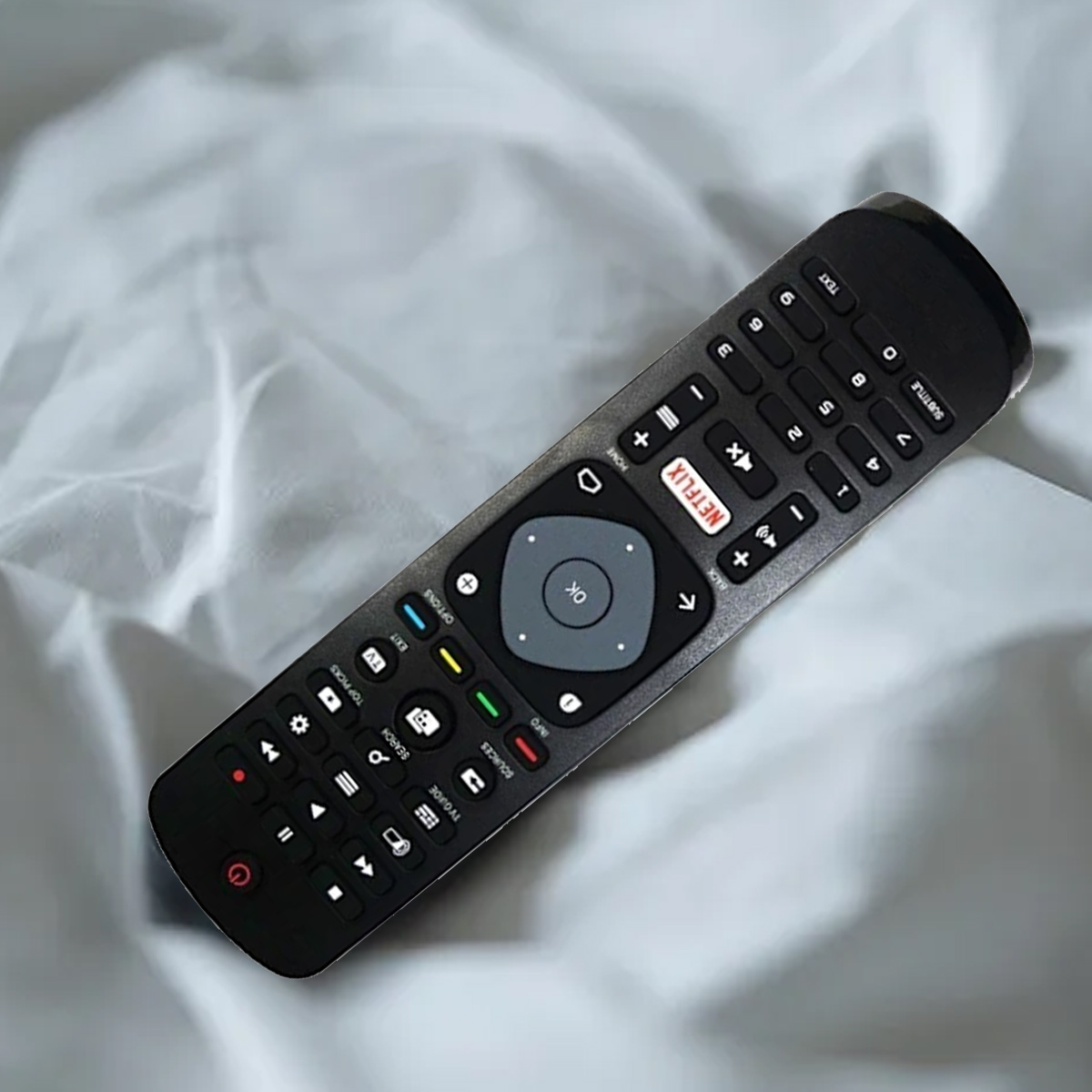 Eine schwarze TV-Fernbedienung mit vielen Tasten liegt auf einem zerknitterten weißen Laken. Tasten umfassen Netflix, Lautstärke und Kanal.