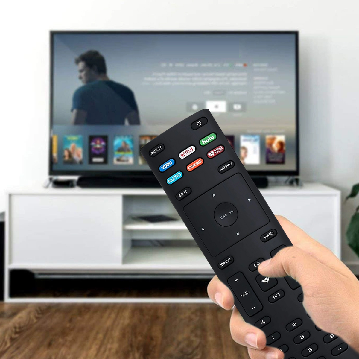 Eine Hand hält eine schwarze Fernbedienung und zeigt auf einen Fernseher. Der Fernseher zeigt ein verschwommenes Bild. Darunter ist ein weißer Schrank.