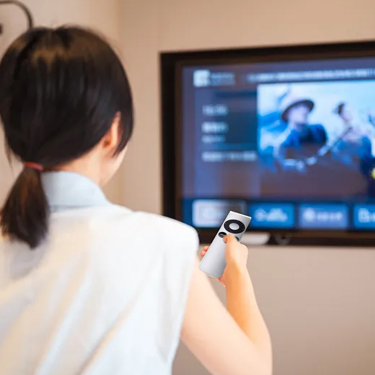 Eine Frau hält eine Fernbedienung vor einem Fernseher. Sie sieht eine Sendung. Der Fernseher ist an der Wand befestigt.