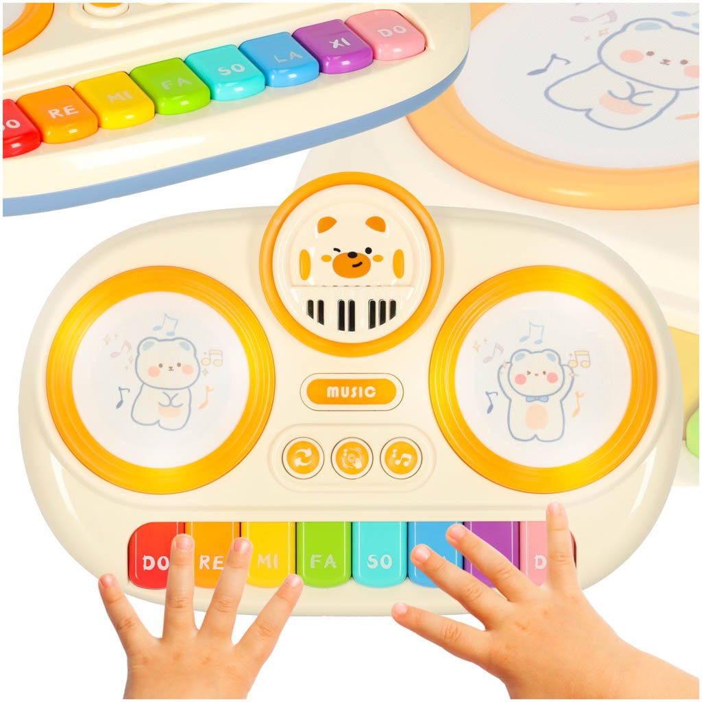 Un piano de juguete para niños con teclas coloridas e ilustraciones de osos. Manos tocando el piano. El fondo muestra otro piano de juguete.