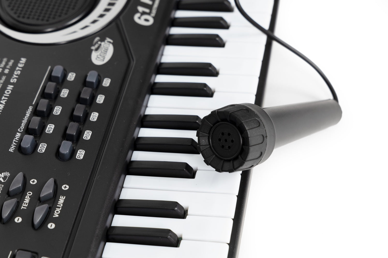 Un teclado negro con teclas blancas y negras, un micrófono descansa sobre las teclas. El teclado tiene botones y etiquetas.