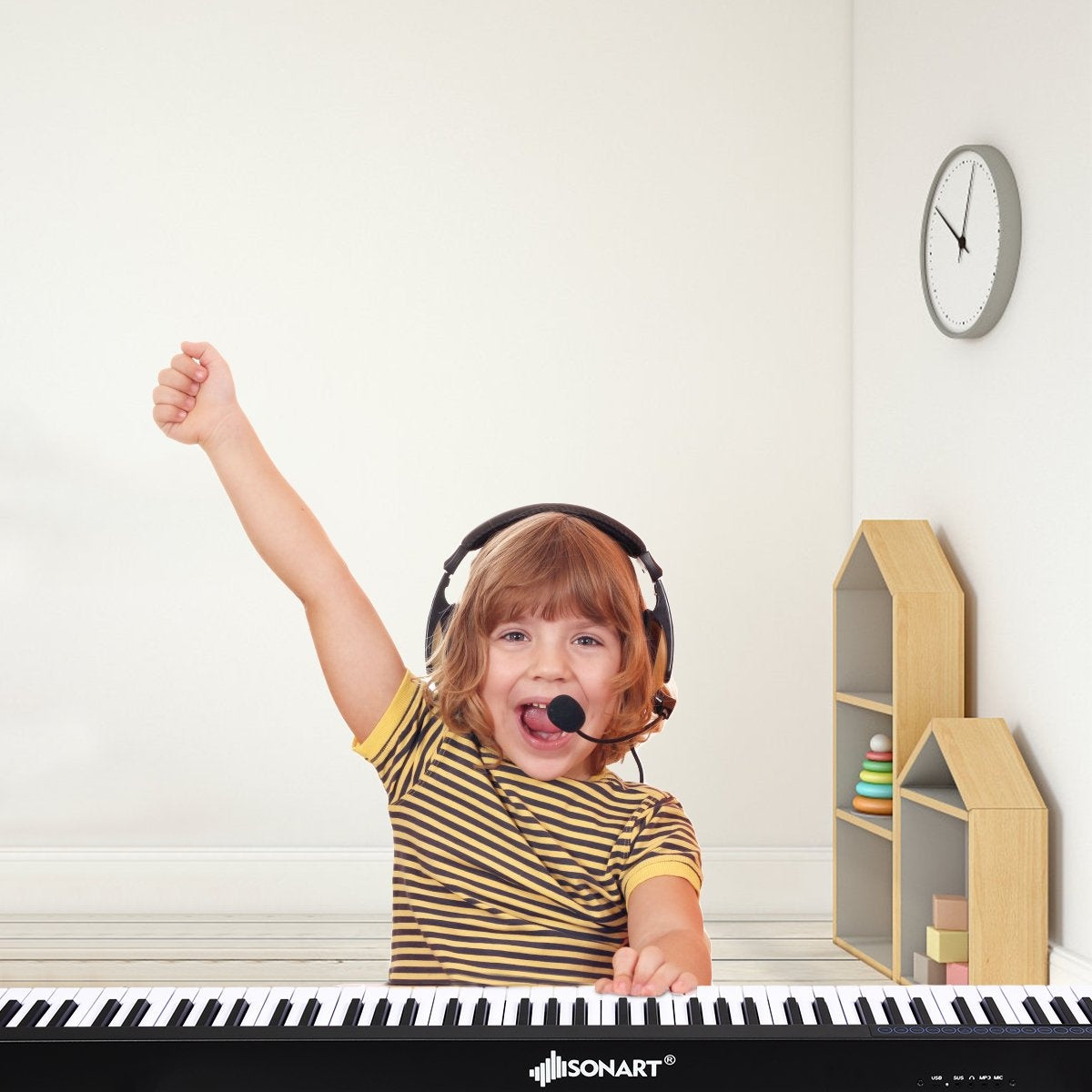 Un niño con auriculares y micrófono toca el piano, levantando un brazo emocionado. Un reloj y estanterías en el fondo.