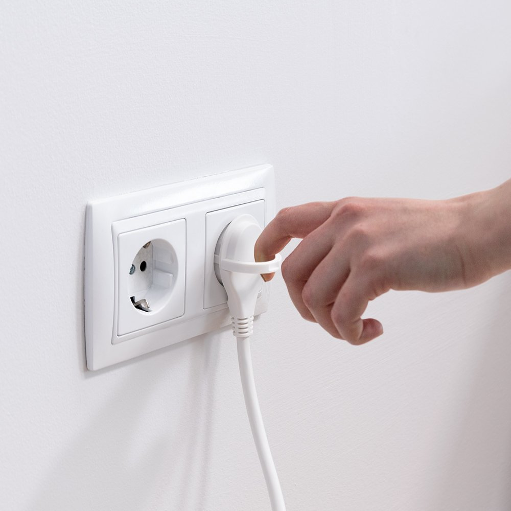 Una mano enchufa un enchufe blanco en un enchufe de pared blanco. La pared es blanca. El enchufe se está insertando.