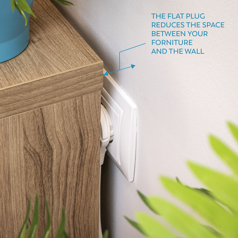 Un enchufe plano está enchufado a un enchufe de pared blanco. Está junto a un armario de madera. El texto dice que el enchufe reduce el espacio.
