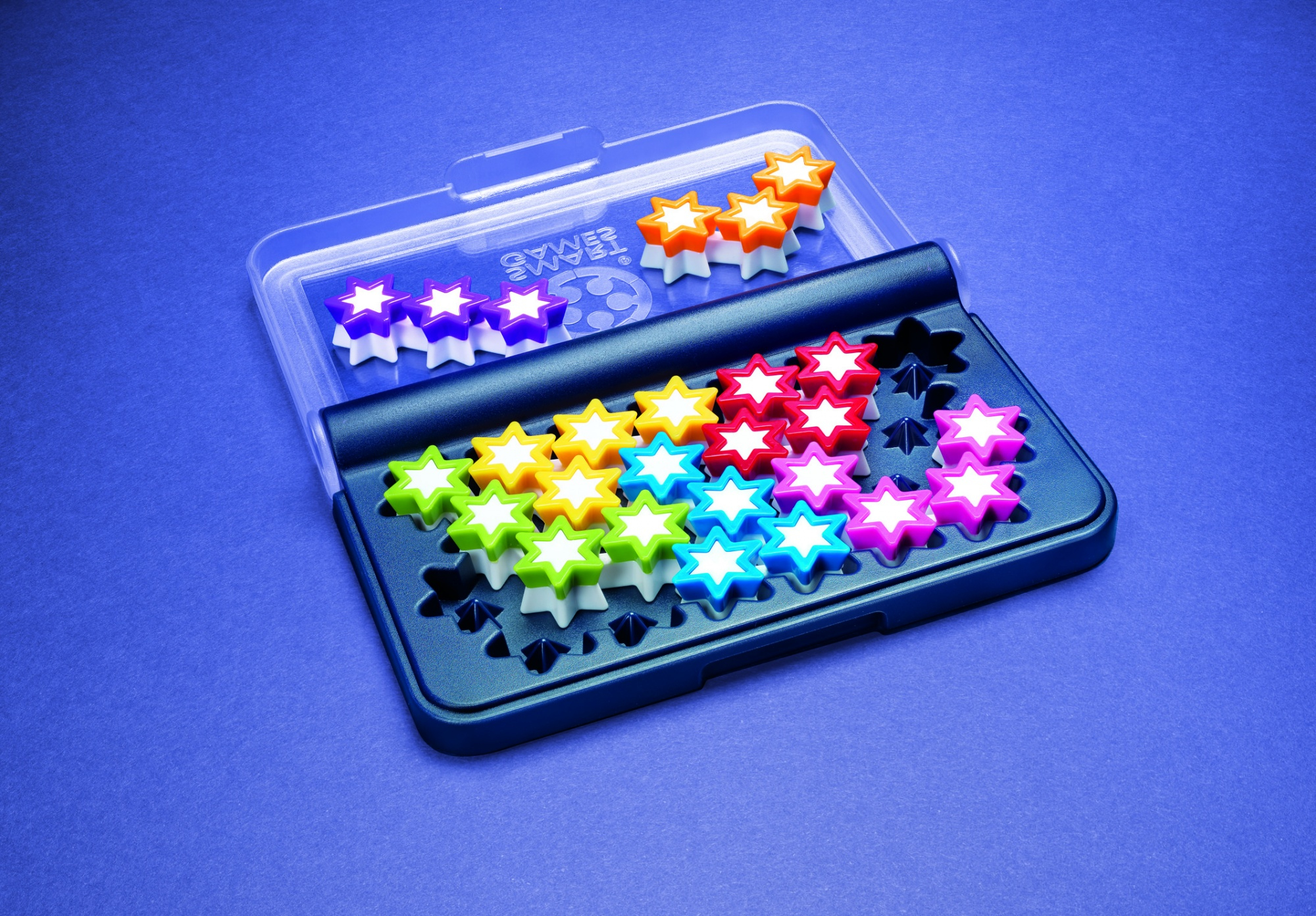 Un juego de rompecabezas con piezas en forma de estrella de varios colores, dispuestas en un estuche sobre una superficie azul. Algunas piezas están en una tapa transparente.