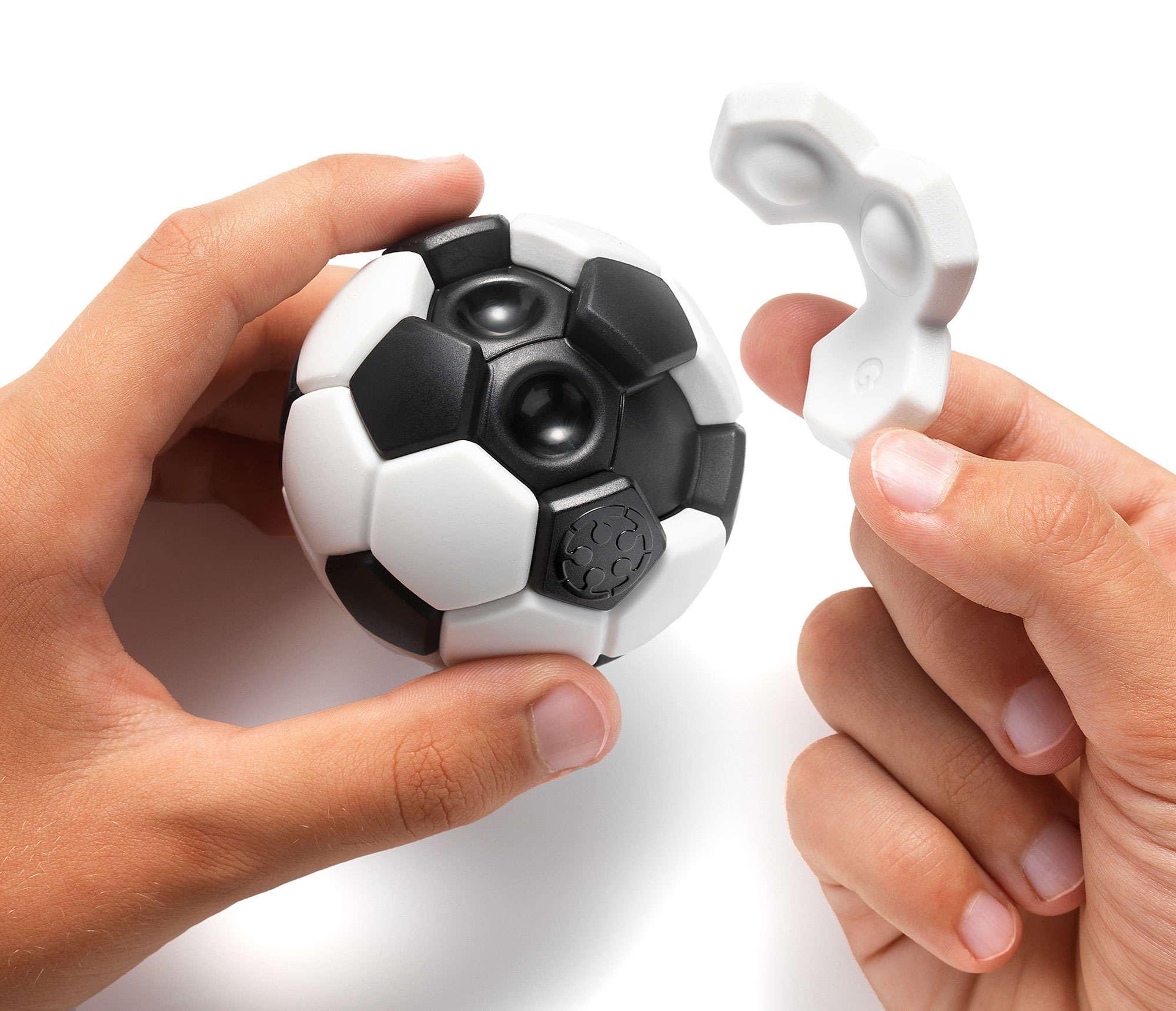 Mani che tengono un giocattolo a forma di pallone da calcio bianco e nero, con un pezzo bianco. Sfondo bianco.