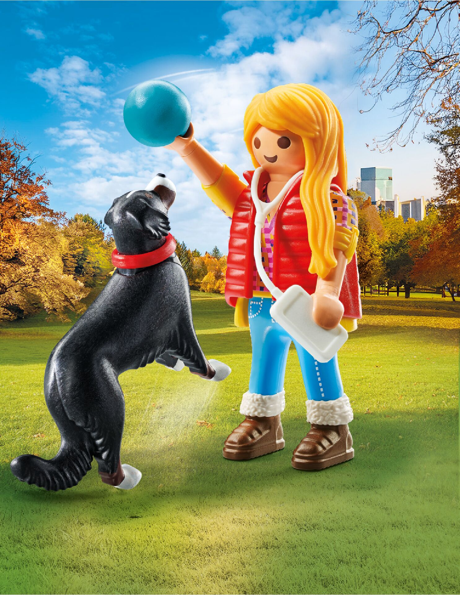 Figurka trzyma niebieską piłkę, pies skacze, by ją złapać. Pies jest czarny z czerwoną obrożą. Jesienny park.