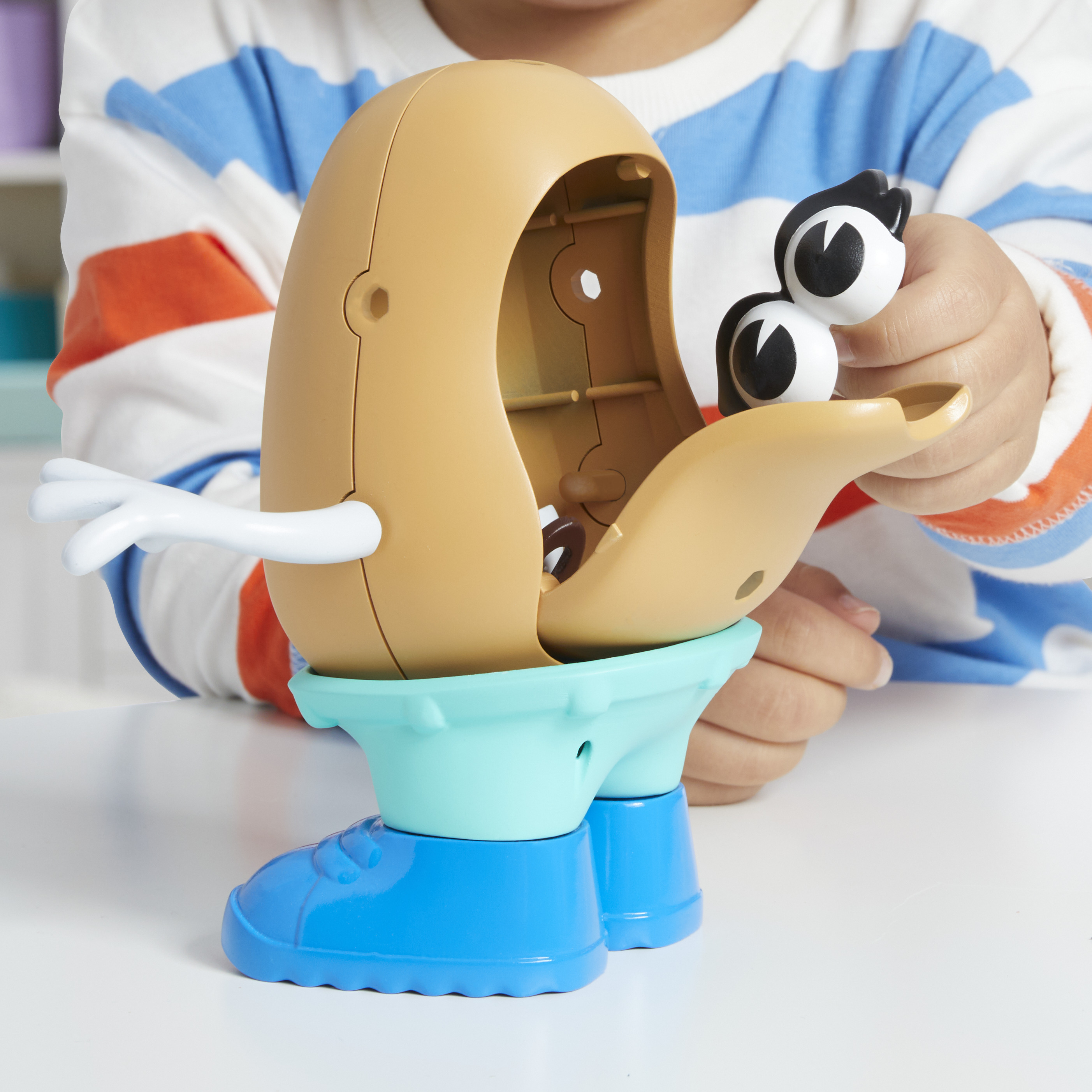 Dziecko trzyma zabawkę Mr. Potato Head. Zabawka jest otwarta, odsłaniając wnętrze. Oczy zabawki są trzymane w dłoni.