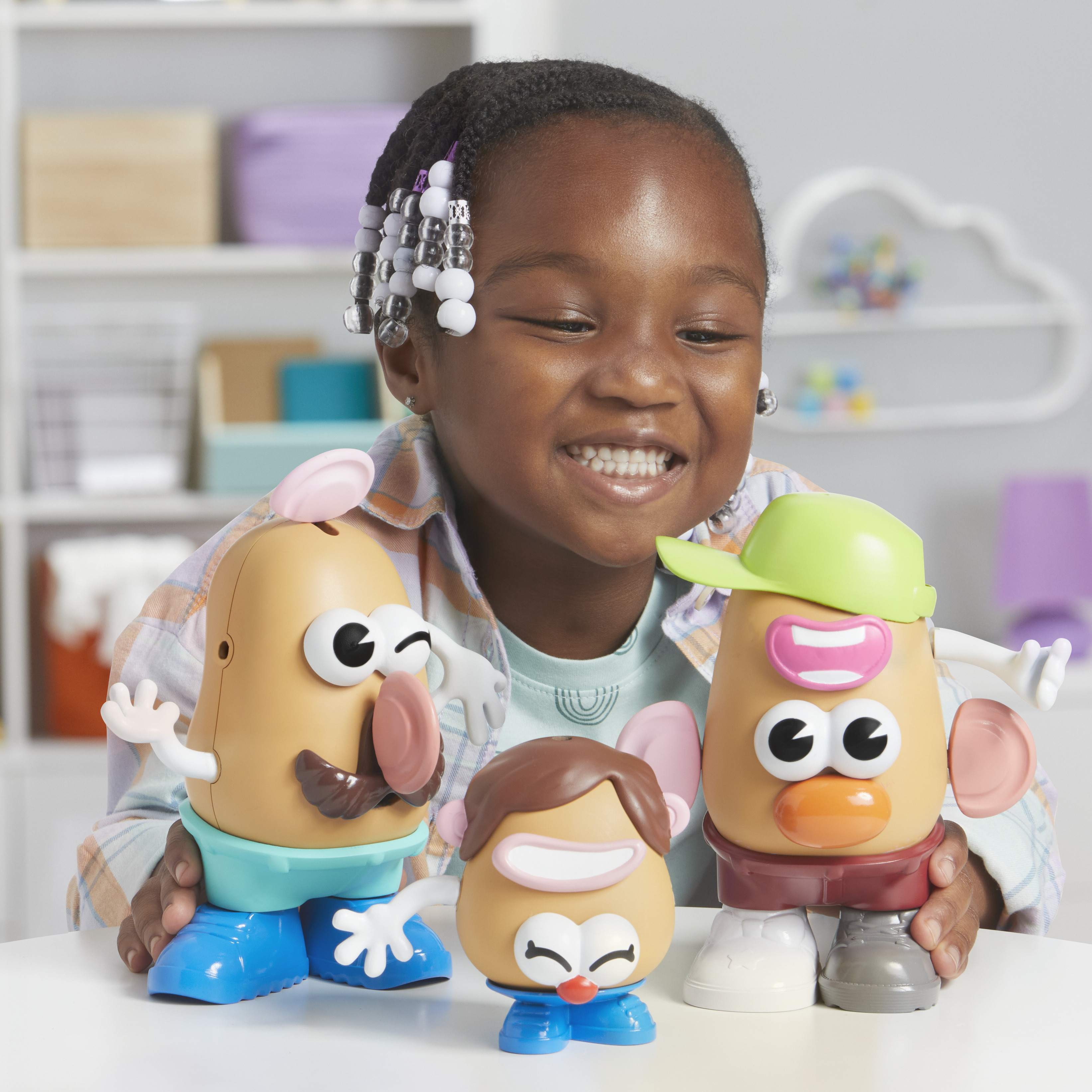 Dziewczyna uśmiecha się do trzech zabawek Mr. Potato Head. Zabawki są na białym stole.