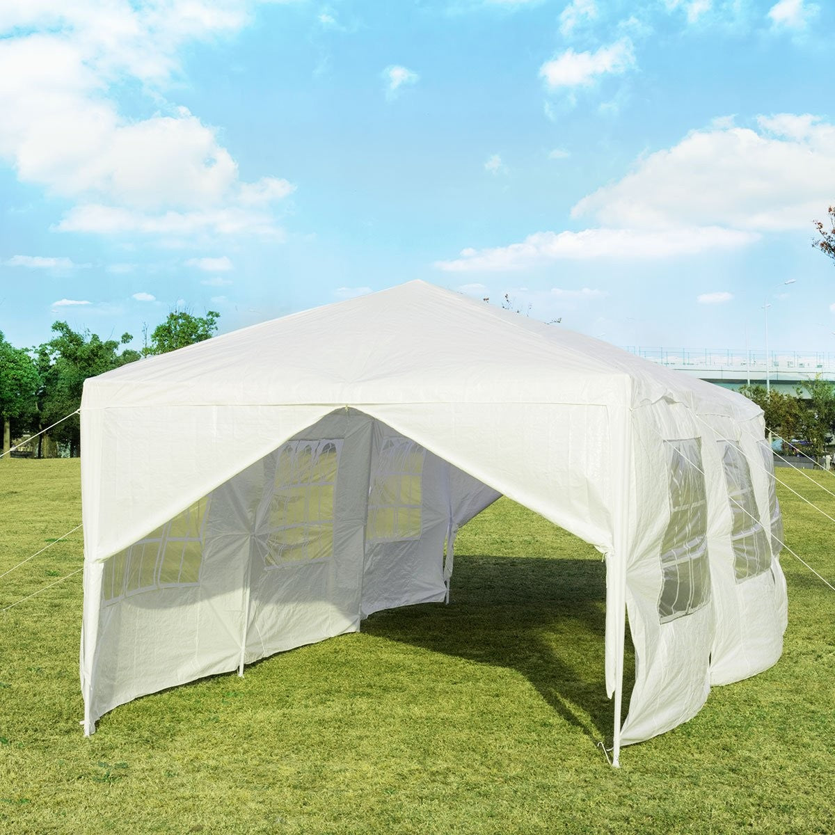Una carpa blanca se instala en un césped verde bajo un cielo azul con nubes. La carpa tiene ventanas en los lados.