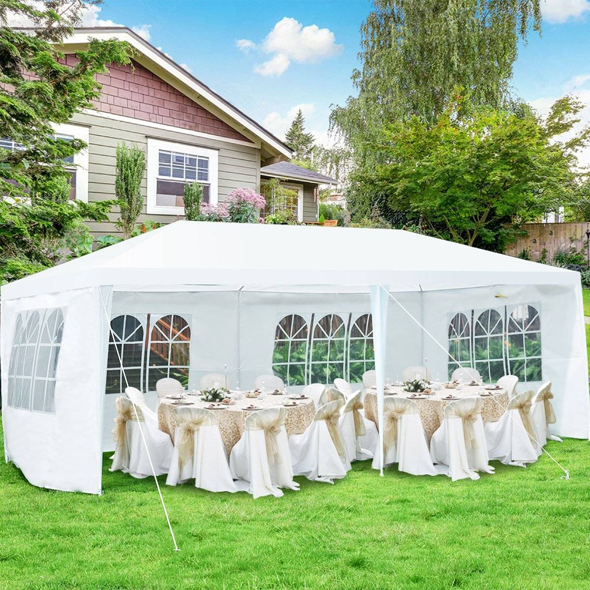 Una carpa blanca instalada sobre césped verde. Dentro hay mesas con manteles blancos y sillas. Una casa y árboles en el fondo.