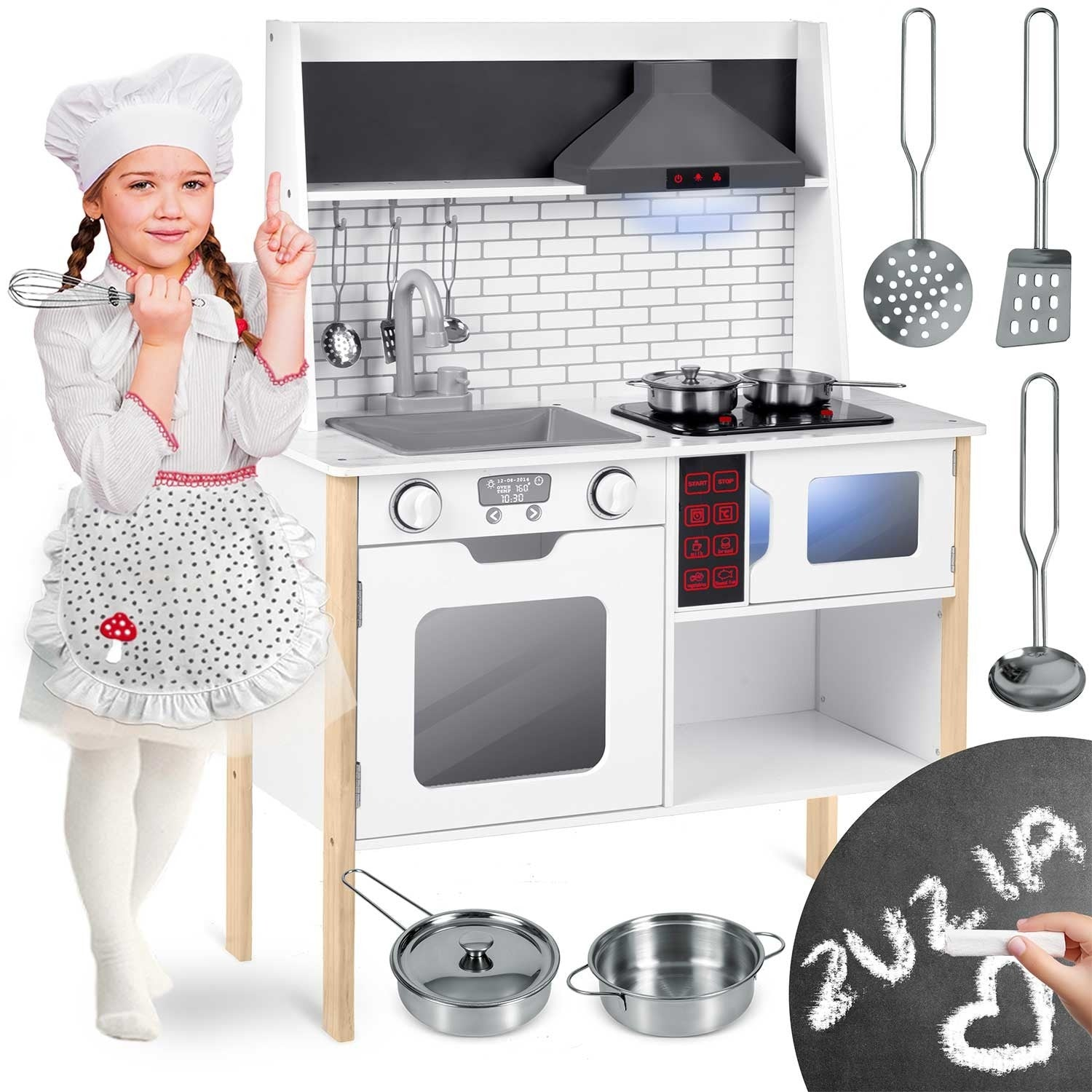 Una niña con un traje de chef está junto a una cocina de juguete. La cocina tiene una estufa, un fregadero y un microondas. Utensilios cuelgan arriba.