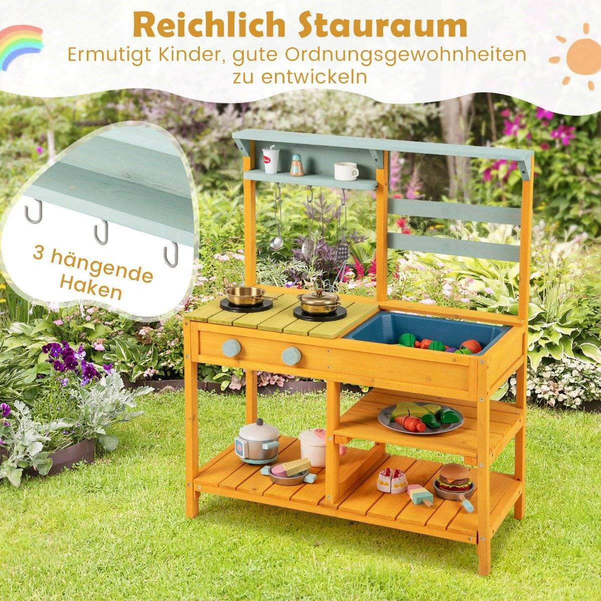 Una cocina de juguete de madera con accesorios, situada en un jardín. Incluye estantes, un fregadero y juguetes de comida, con texto en alemán.
