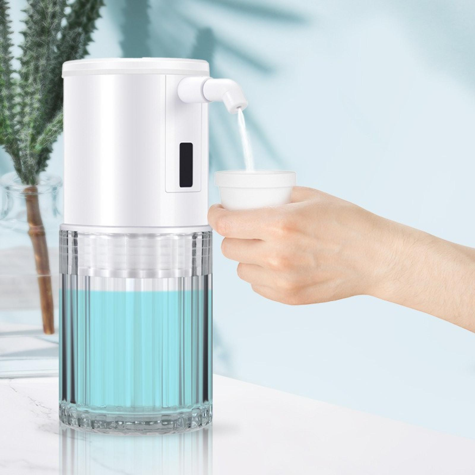 Ein weißer Seifenspender gibt Flüssigkeit in einen weißen Becher ab, der von einer Hand gehalten wird. Blaue Flüssigkeit ist sichtbar.