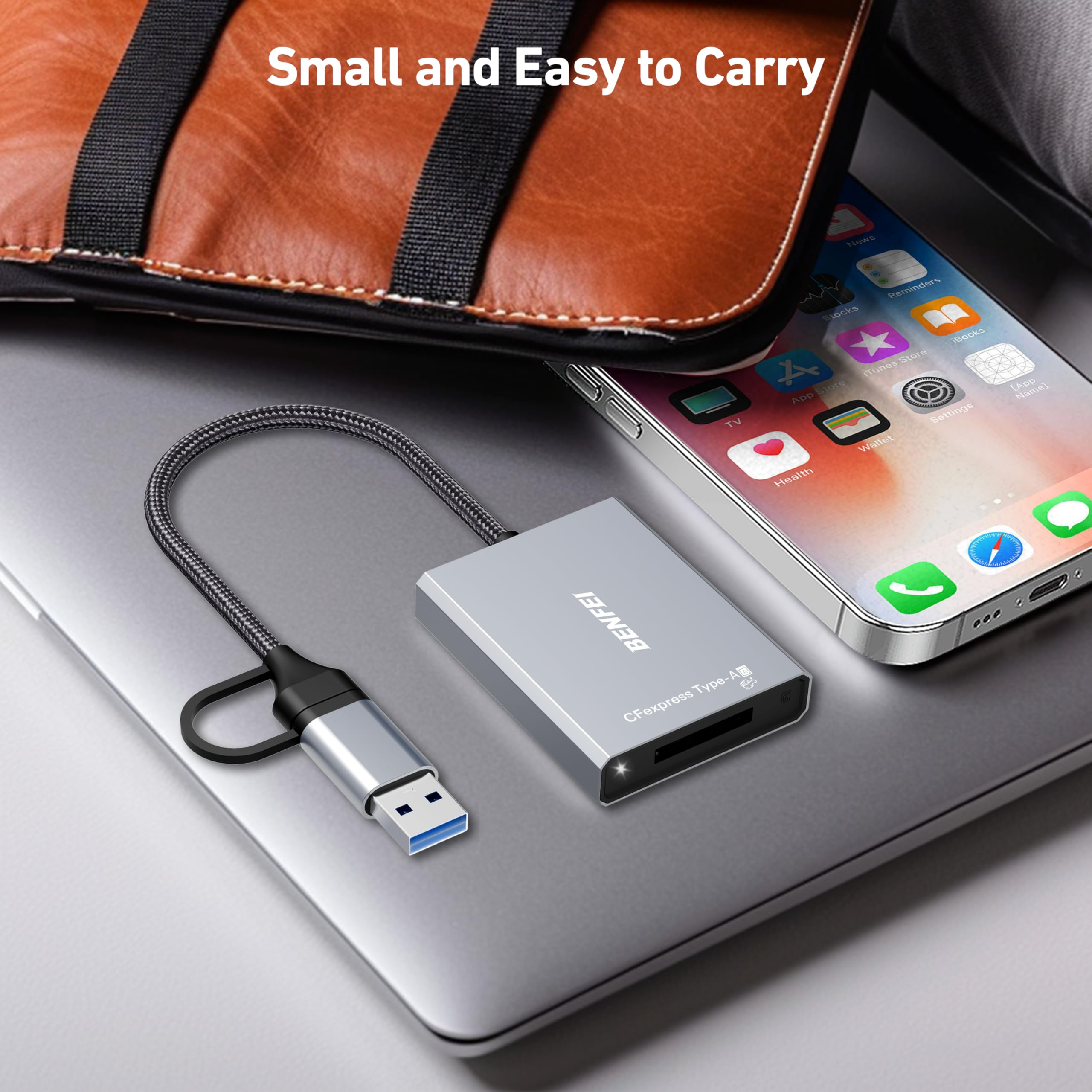 Ein silbernes Kartenlesegerät, das mit einem Laptop verbunden ist, mit einem Telefon und einer braunen Tasche im Hintergrund.