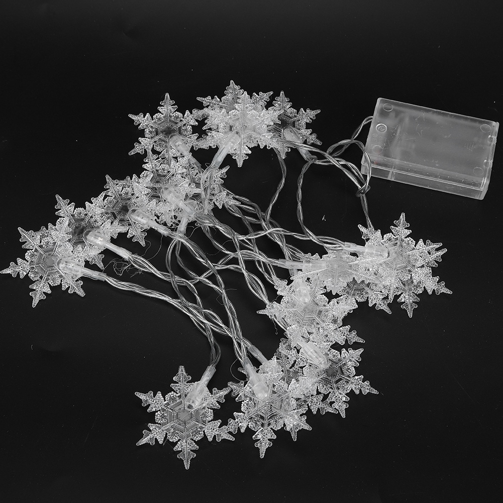 Lichterkette aus durchsichtigen Schneeflocken auf schwarzem Untergrund, mit einer durchsichtigen Batteriebox.