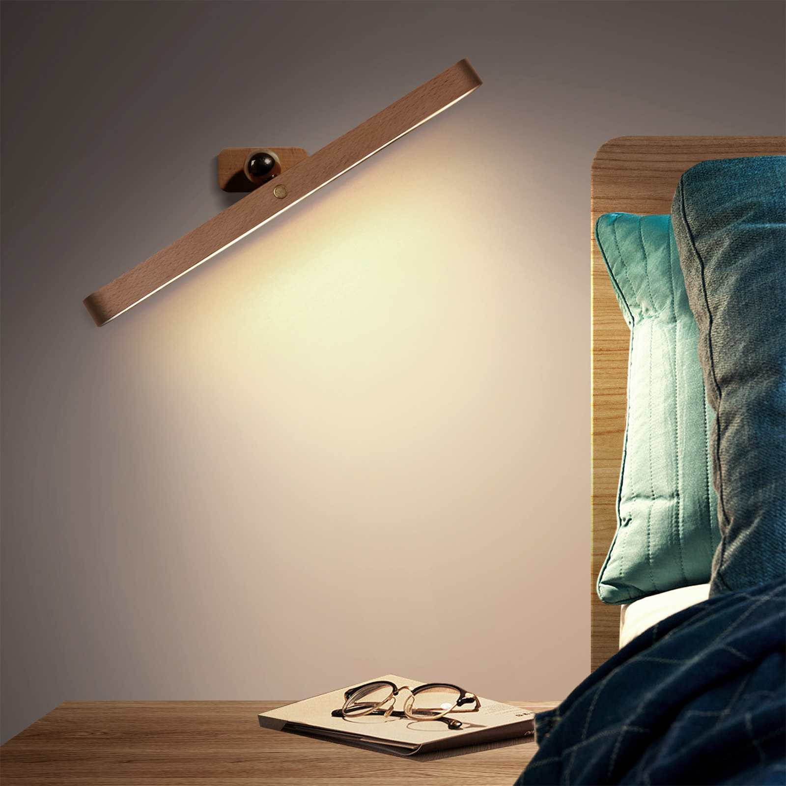 Eine hölzerne Wandleuchte beleuchtet einen Nachttisch mit Brille und Buch. Rechts ein Bett mit Kissen.