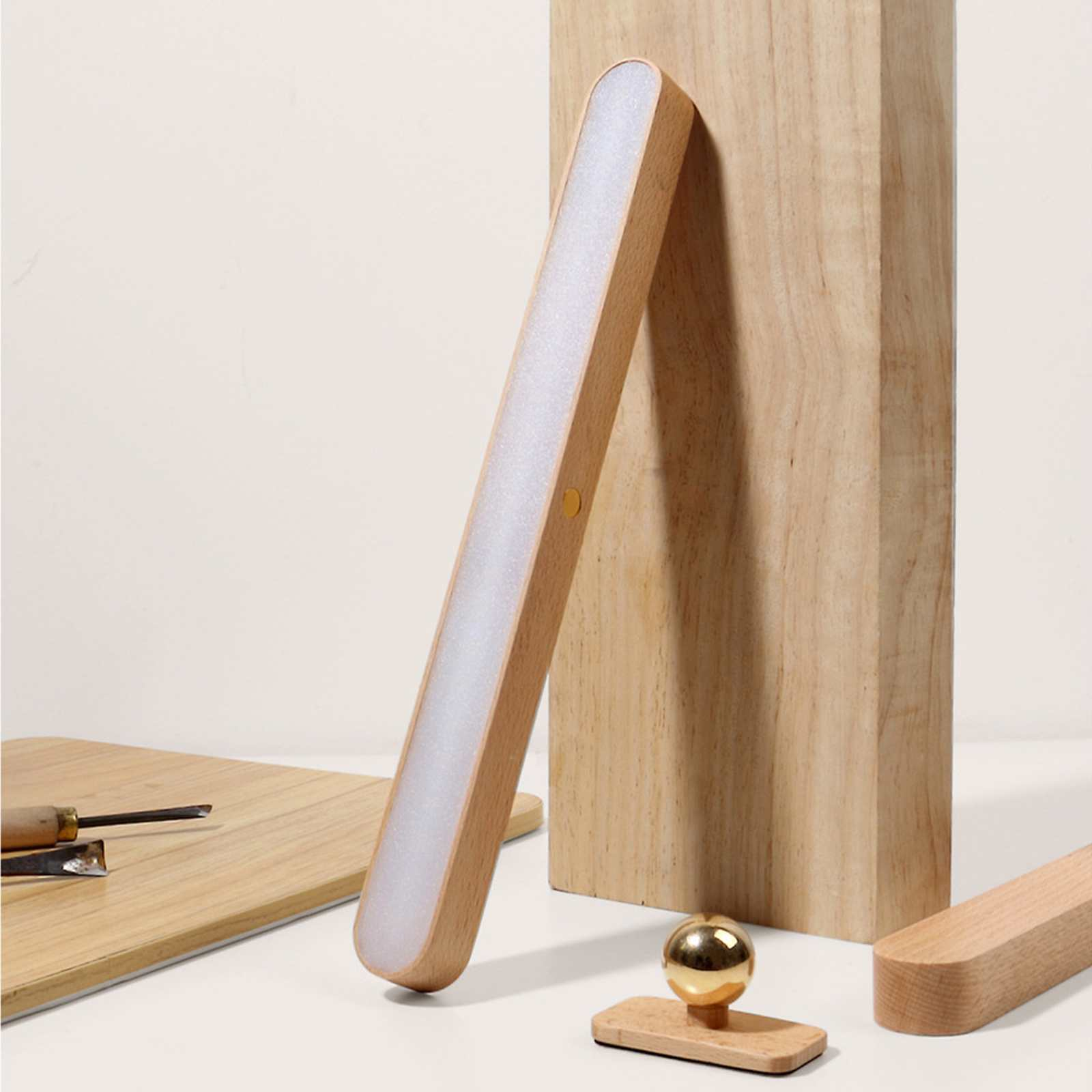 Eine Holzlaterne mit Leuchtleiste lehnt an einem Holzblock. Eine goldene Kugel sitzt auf einem Holzsockel.
