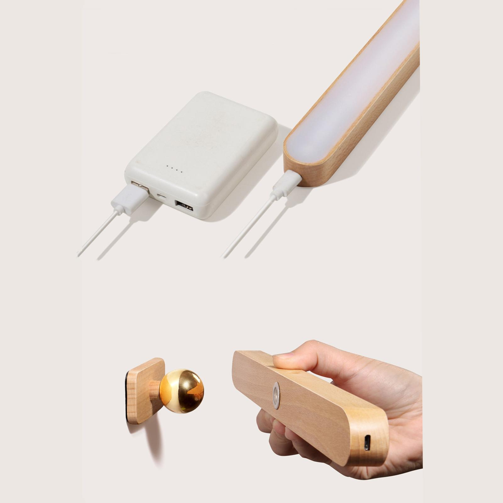 Das Bild zeigt eine weiße Powerbank und eine Holzlampe, die aufgeladen werden. Außerdem einen Türstopper aus Holz und eine Hand, die ein Holzgerät hält.