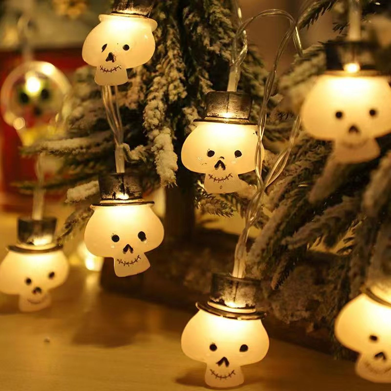 Lichterkette mit Totenkopf-Glühbirnen mit Zylinder auf einem kleinen, künstlichen Baum mit verschneiten Ästen.