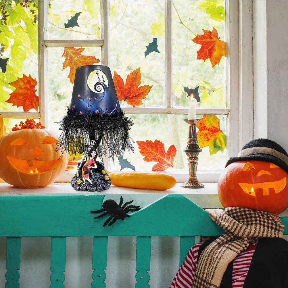 Halloween-Szene: Kürbisse, eine Lampe und eine Kerze auf einer Fensterbank, dekoriert mit Blättern und Fledermäusen. Eine Spinne liegt auf der Bank.