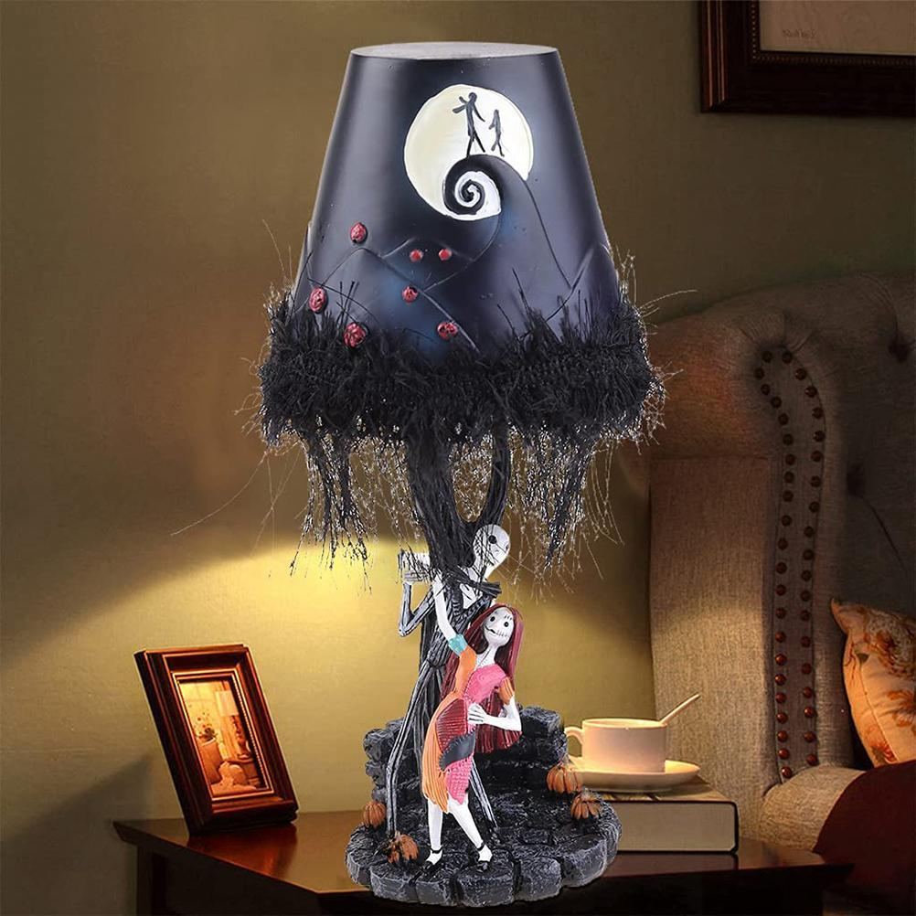 Eine „Nightmare Before Christmas“-Lampe. Figuren von Jack und Sally stehen unter einem schwarzen Lampenschirm mit Mond- und Hügeldesign. Im Hintergrund sind ein Tisch und ein Bett zu sehen.