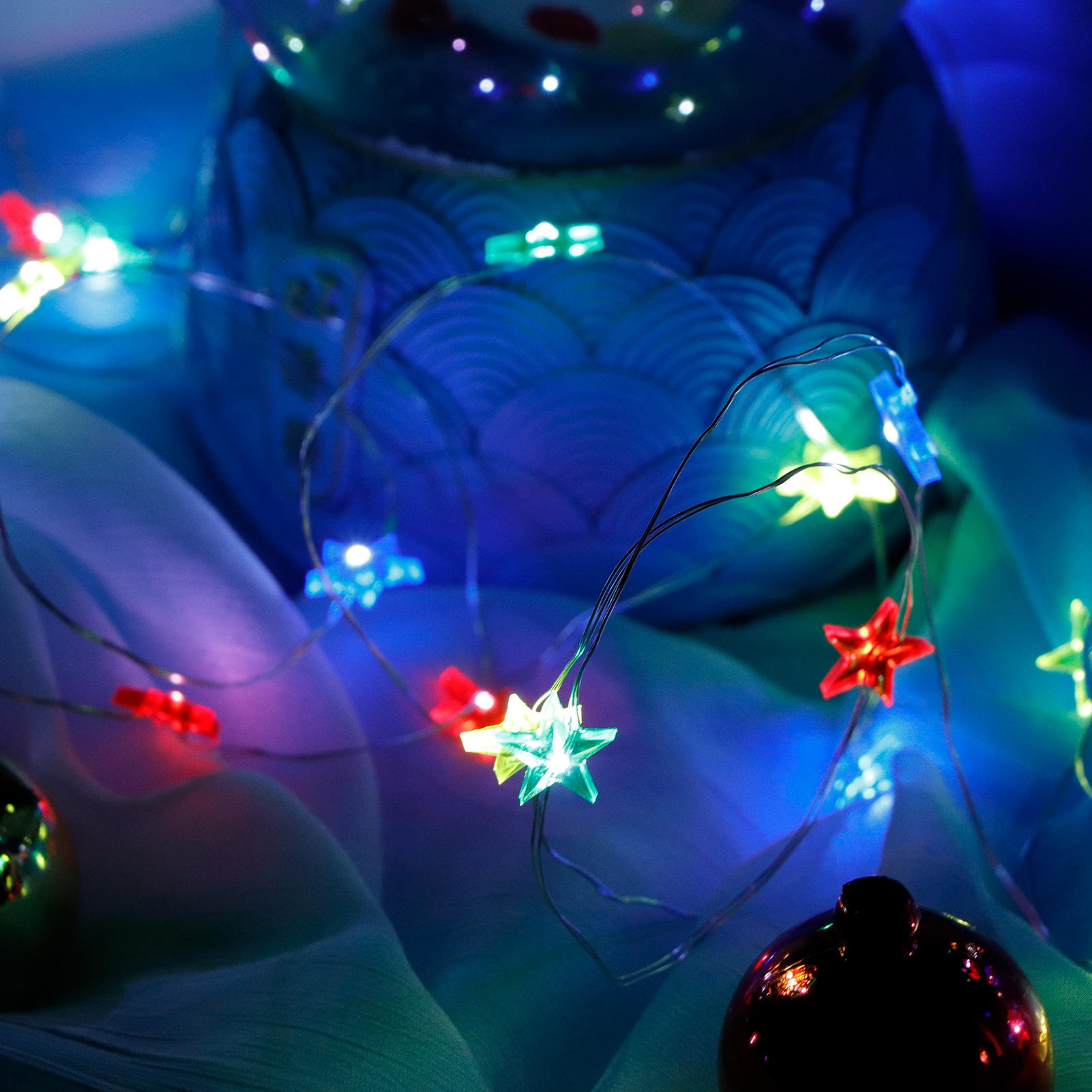 Ein blauer Keramikbehälter mit sternförmigen Lichtern. Rote, grüne und blaue Lichter an einem Draht, mit dunklem Ornament.