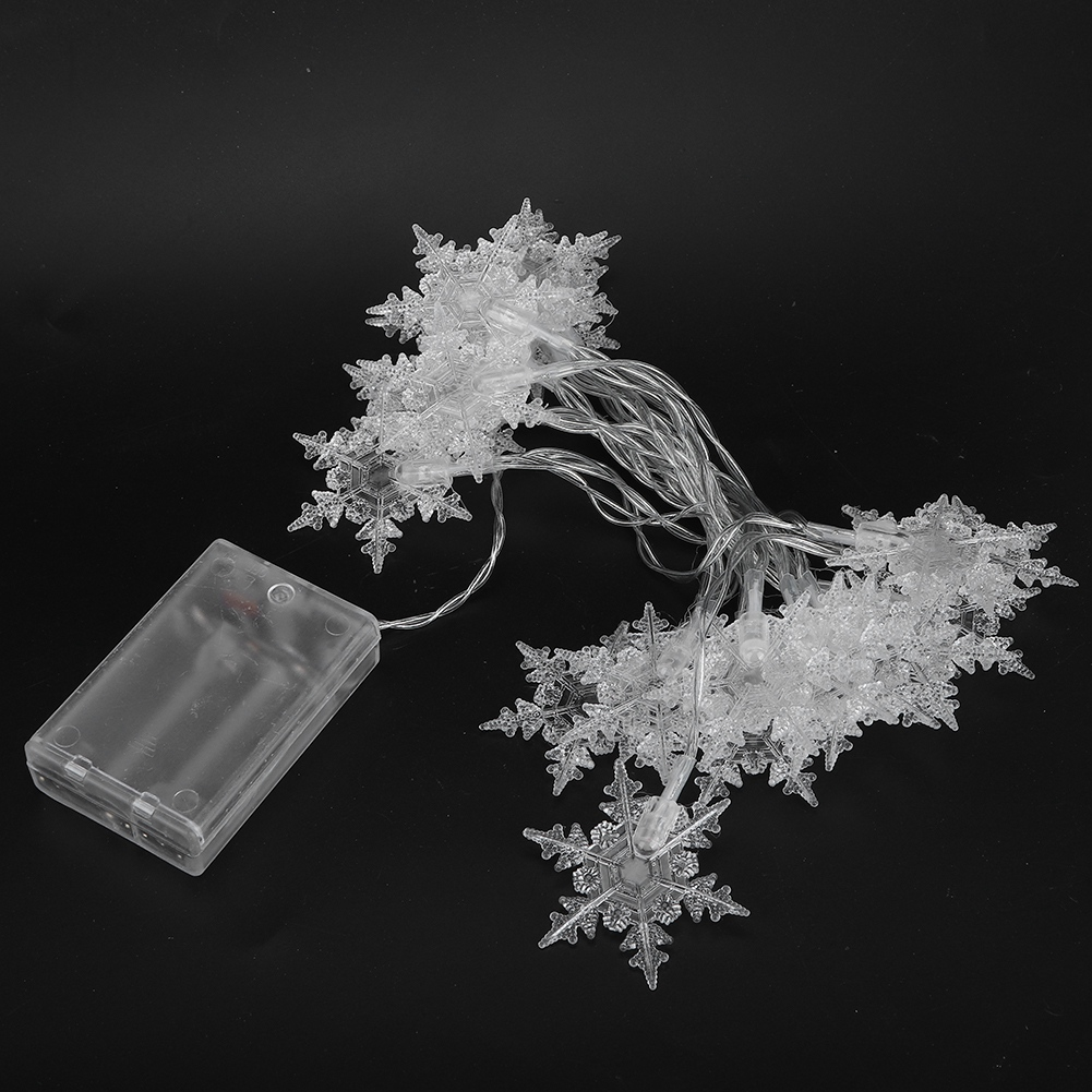 Klare Schneeflockenlichter und ein Akkupack liegen auf einer schwarzen Oberfläche. Die Lichter sind geclustert, mit dünnen Drähten verbunden.