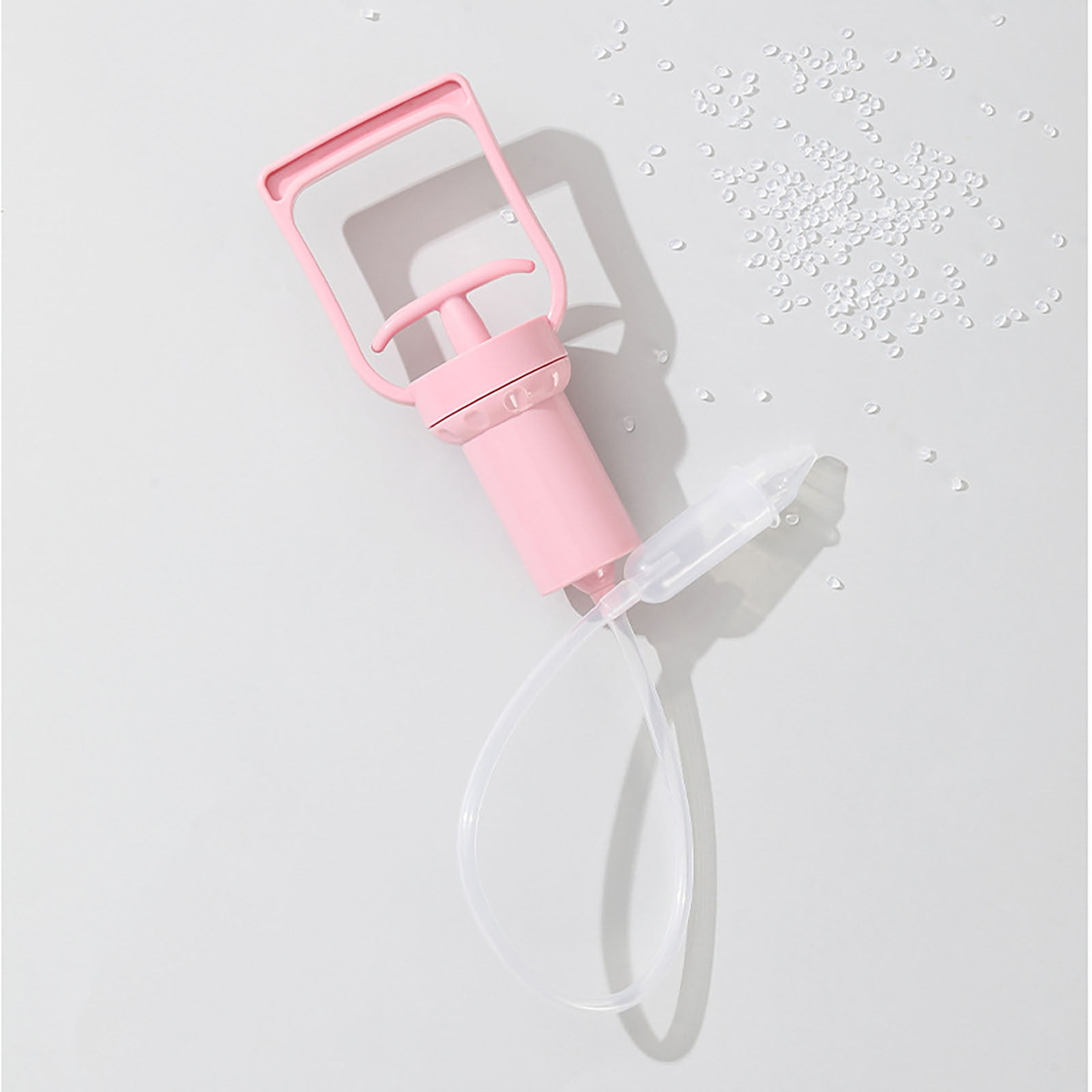 Eine rosa Brustpumpe liegt auf einer weißen Oberfläche. Kleine weiße Kügelchen liegen im Hintergrund verstreut.