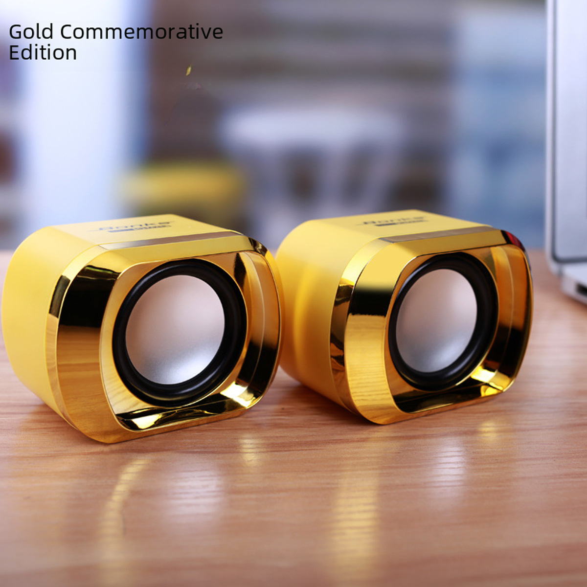Zwei gelbe und goldene Lautsprecher auf einem Holztisch. Die Lautsprecher sind nach vorne gerichtet. Der Hintergrund ist verschwommen.